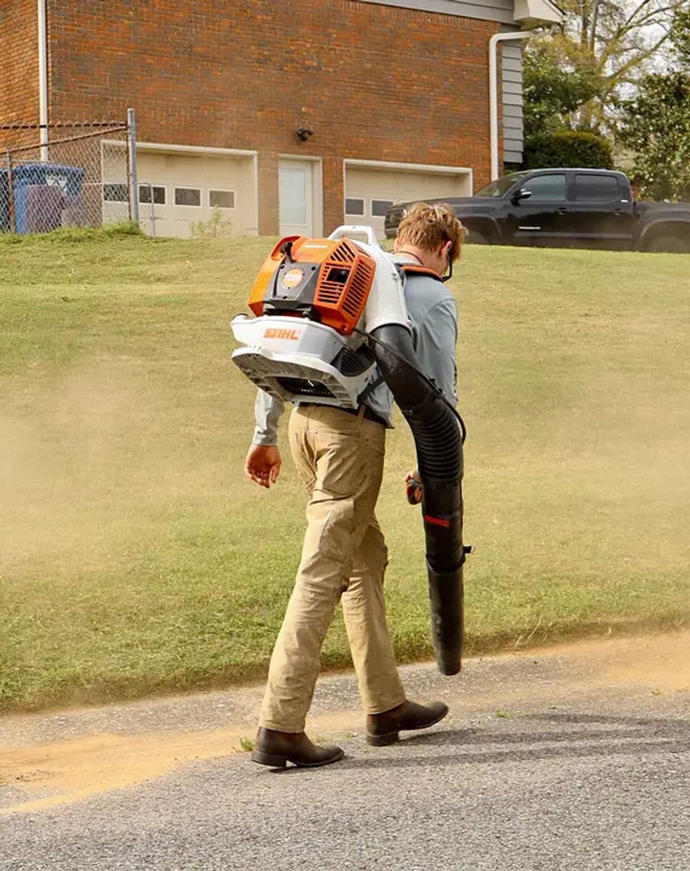 Man using a Stihl backpack leaf blower on a lawn, clearing leaves and debris.