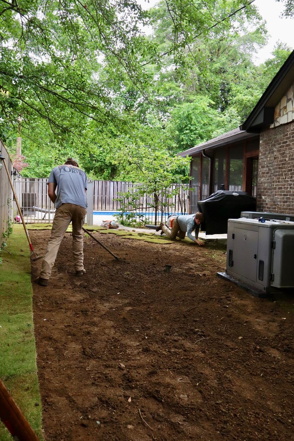 Landscapers preparing soil in a residential backyard for planting and garden renovation.