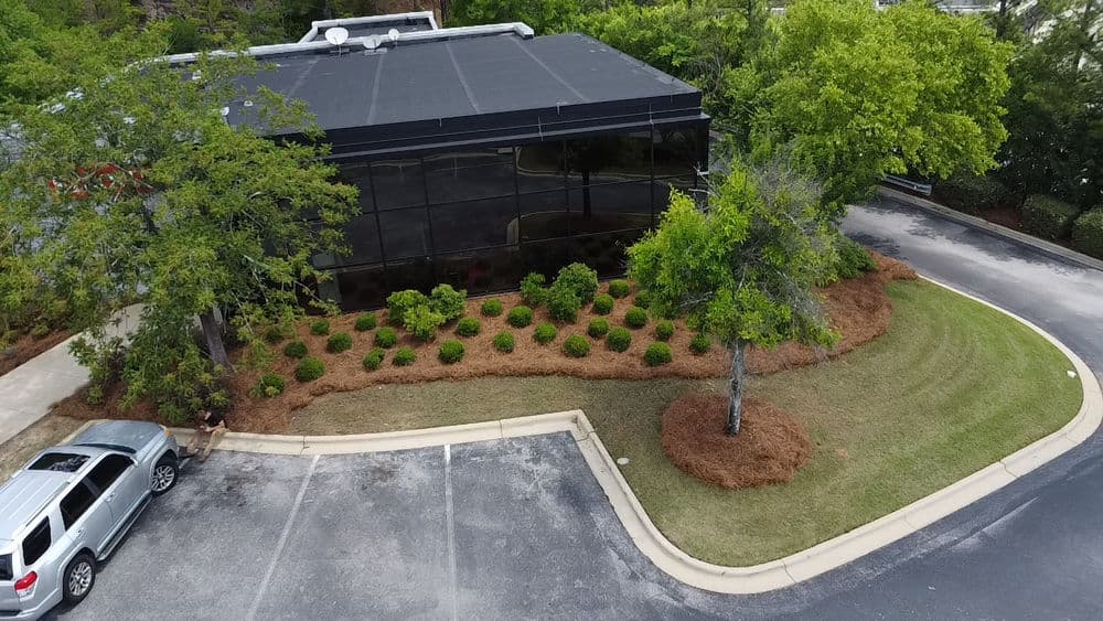 Aerial view of a modern building with landscaped gardens and a parked silver SUV.