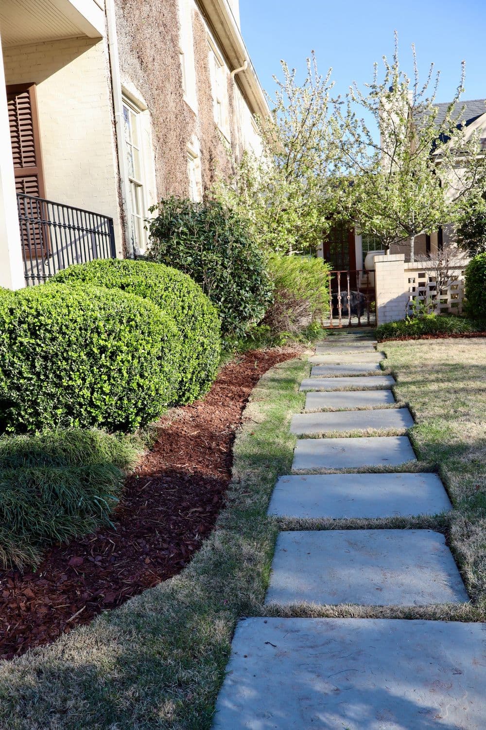 Stone pathway leading through landscaped yard with shrubs and flowering trees.